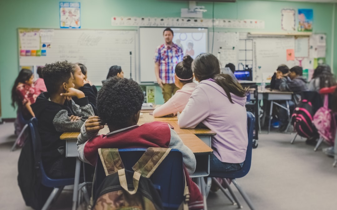 A SPED teacher stands at the front of a classroom with a diverse group of students all paying attention.